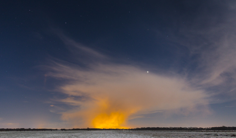 Licht van kassen schijnt in de nacht op bewolking